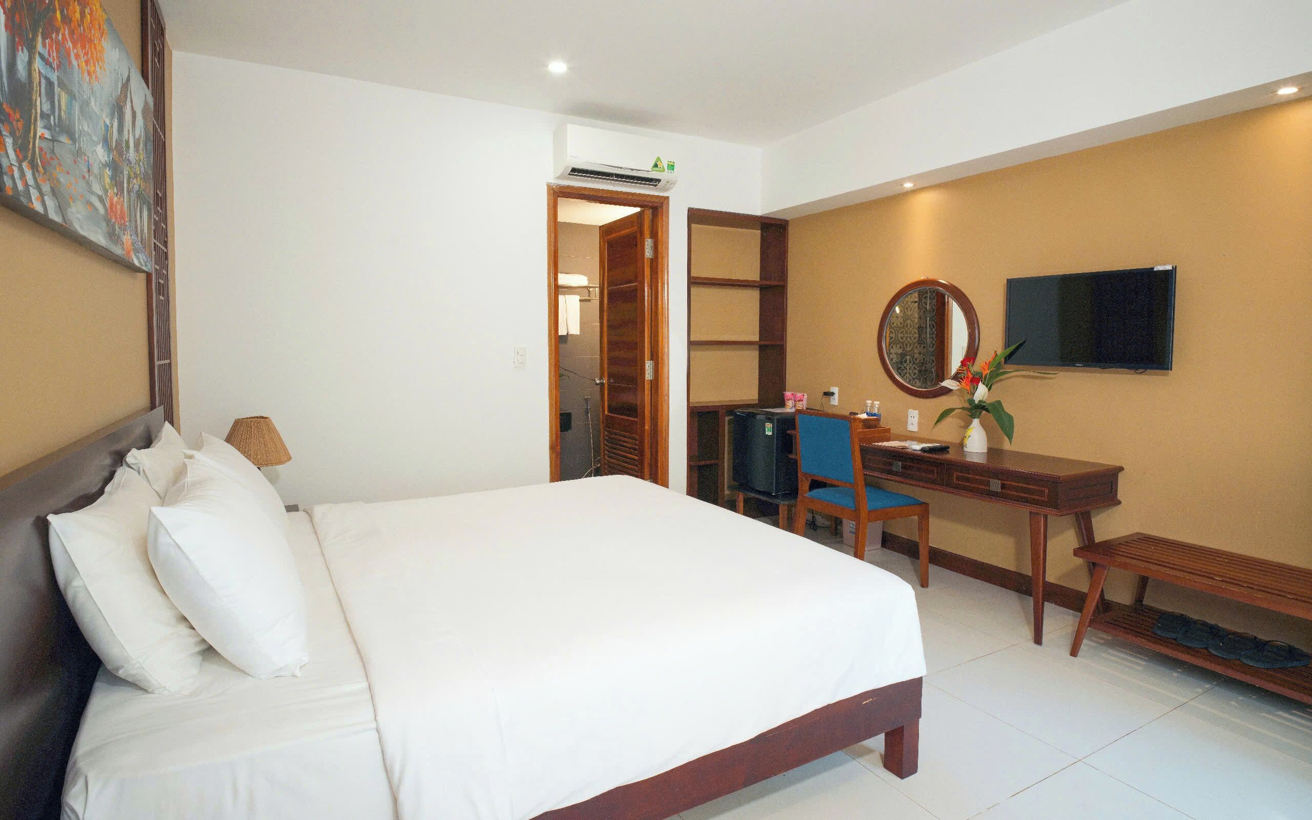 A hotel room with a bed, a desk, a chair, a TV, and a painting on the wall.