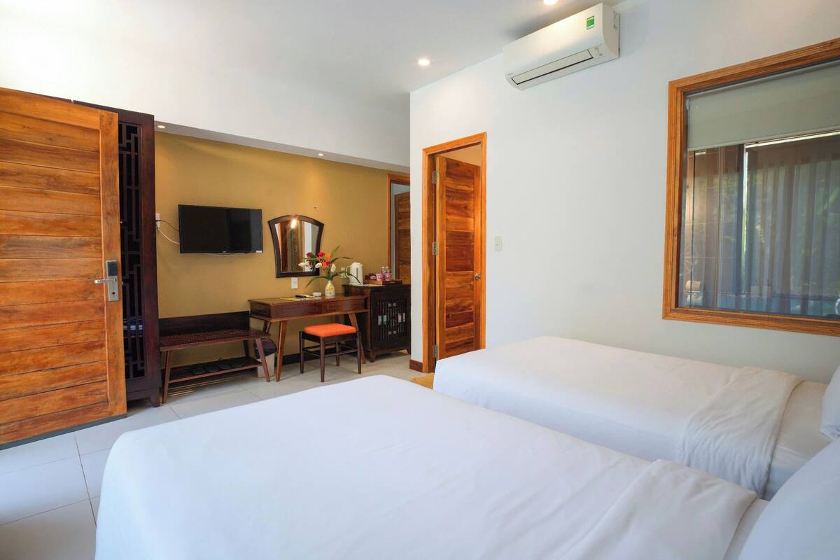 A hotel room with two beds, a desk with a chair, a television, and a large window.
