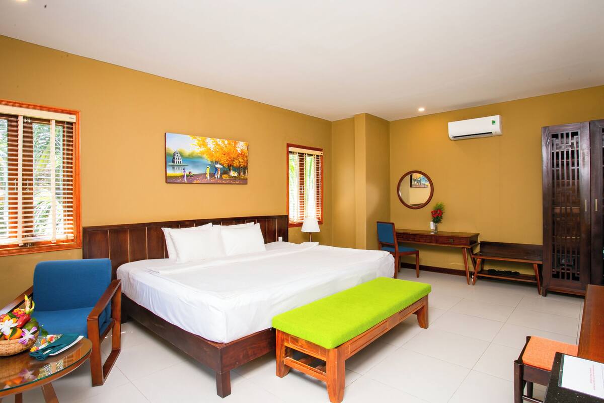 A hotel room with a bed, a desk, a chair, a bench, and a wardrobe.