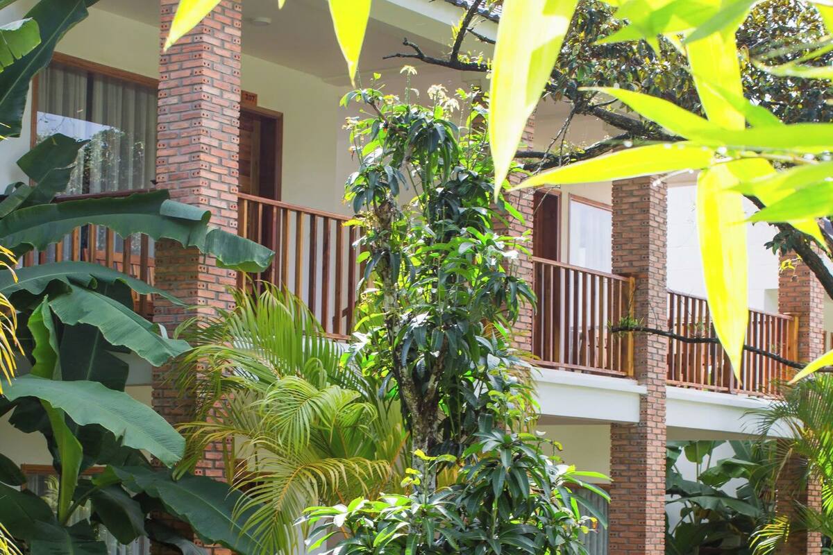 A two-story building with a brick facade, a balcony, and a well-maintained garden with various plants and a stone pathway.