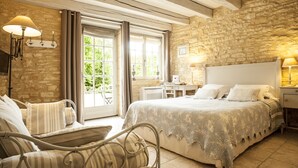 Un dormitorio con pared de piedra, una cama grande con ropa blanca, un escritorio con silla y una ventana con cortinas.