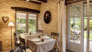 Un comedor con paredes de piedra, una mesa dispuesta para dos personas y vistas al jardín a través de un ventanal.