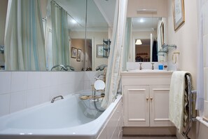 A bathroom with a bathtub, a sink, a mirror, and a towel rack.