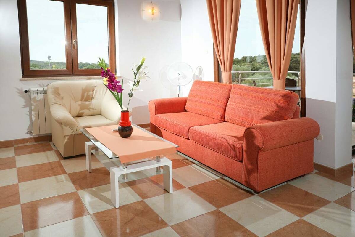 A living room with a beige sofa, an orange sofa, a small table, and a vase with flowers.