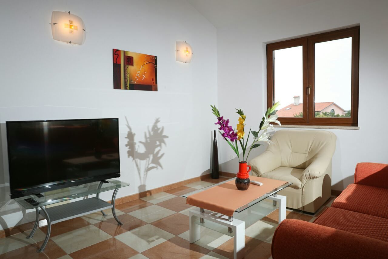 A modern living room with a flat-screen TV on a glass table, a beige sofa, a red sofa, and a window with a view of buildings.