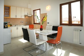 Une cuisine moderne avec des meubles blancs, une table à manger entourée de quatre chaises et une fenêtre donnant sur des immeubles.