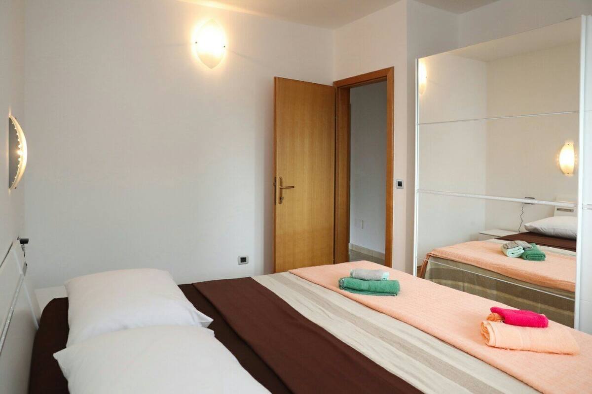 A hotel room with two beds, a wooden door, a mirror, and a wall-mounted light fixture.