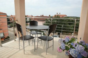 Un balcon avec une table et des chaises, une balustrade et une vue sur des bâtiments et de la verdure.