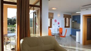 Ein Wohnzimmer mit einer Couch, einem Esstisch mit Stühlen und einem durch eine offene Tür einsehbarer Küchenbereich.