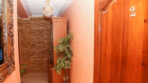 A hallway with a wooden door marked with the number 2, a potted plant, and a brick wall. - Tamraght House (Aourir)