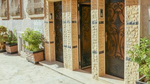 A building facade with ornate metal doors and windows, potted plants, and a textured stone wall. - Tamraght House (Aourir)