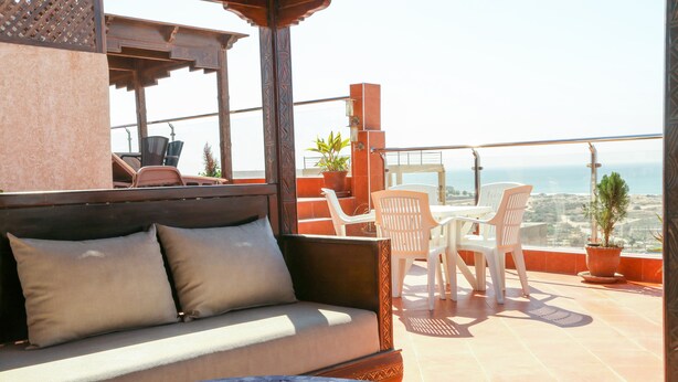 A balcony with a sofa, chairs, and potted plants. - Tamraght House (Aourir)