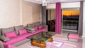 A modern living room with a glass coffee table, a grey sofa with pink cushions, and a pink ottoman. - Tamraght House (Aourir)