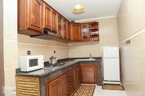 A kitchen with wooden cabinets, a microwave, a stove, and a refrigerator. - Tamraght House (Aourir)