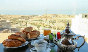 A table with pastries, a teapot, and a glass of tea, overlooking a scenic view. - Tamraght House (Aourir)