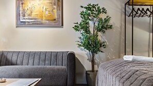 Uma sala de estar moderna com um sofá cinza, uma mesinha, uma planta em vaso e uma cama com cobertor cinza.