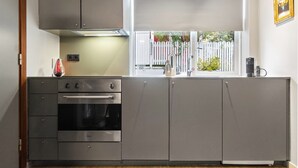 Cozinha com forno embutido, pia e janela com vista para um cercado branco e vegetação.