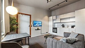 Uma sala de estar moderna com um sofá cinza, uma mesa de jantar e uma televisão.