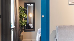 Quarto de hotel com um espelho grande, um vaso de planta, uma toalha e uma poltrona cinzenta.