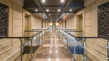 Un largo pasillo bien iluminado, con suelo de mármol y barandillas de vidrio, que conduce a una escalera.
