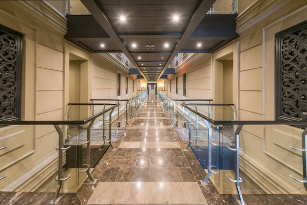 Un largo pasillo bien iluminado, con suelo de mármol y barandillas de vidrio, que conduce a una escalera.