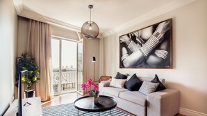Ein modernes Wohnzimmer mit einer Couch, einem Couchtisch mit Blumenvase, einem großen abstrakten Gemälde und Blick auf die Stadt vom Balkon aus.