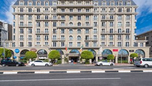 Ein großes, mehrstöckiges Hotel im klassischen Stil, mit einem zentralen Eingang, zahlreichen Balkonen und einer auffälligen Flaggenpräsentation.