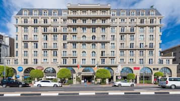 Un hotel grande de varios pisos con un estilo arquitectónico clásico, que cuenta con una entrada central, múltiples balcones y una destacada exhibición de banderas.