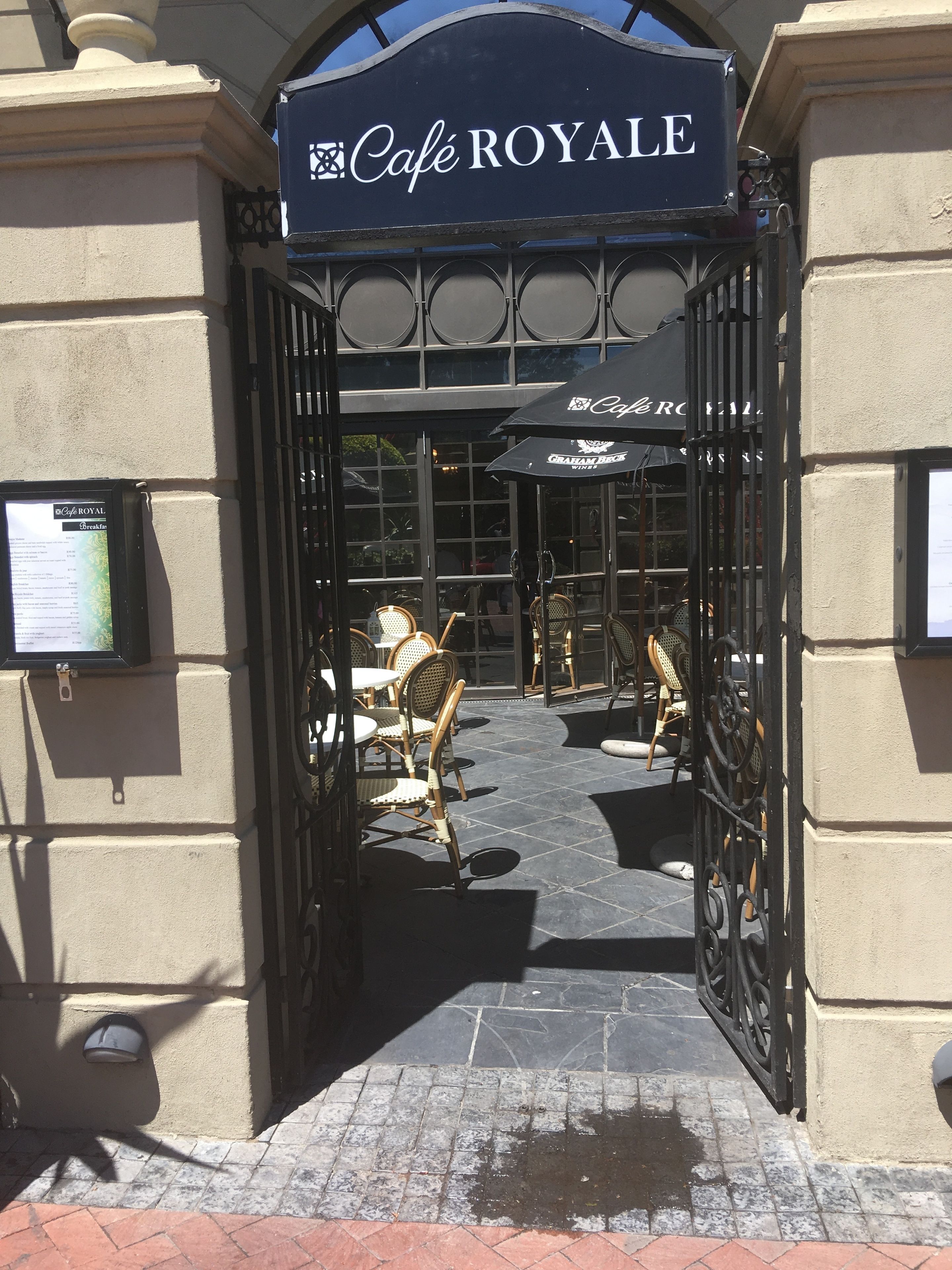 Entrada al Café Royale, con un portón negro y zona de estar al aire libre.