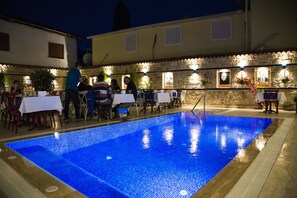 An outdoor swimming pool with a stone wall and tables and chairs around it. - Kervan Hotel (Antalya)