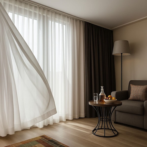 A modern living room with a sofa, a round table with a lamp, and sheer curtains.