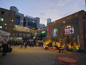 Una piazza cittadina con posti a sedere all'aperto, un caffè e un edificio con insegne illuminate.