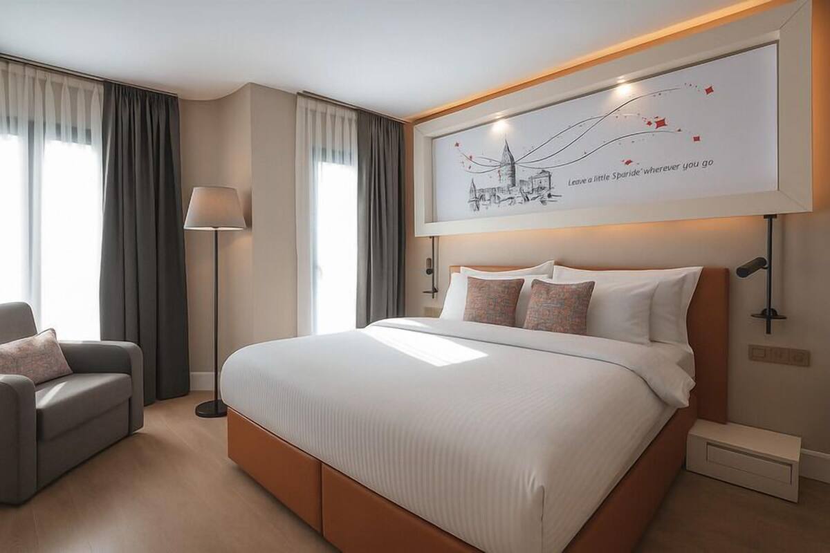 Habitación de hotel moderna con una cama grande, un sofá, una lámpara de pie y una obra de arte enmarcada en la pared.
