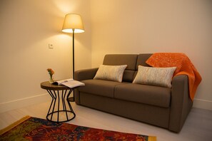 A room with a sofa, a lamp, a small table with a book and flowers, and a colorful rug. - Sparkle Hotel (Istanbul)