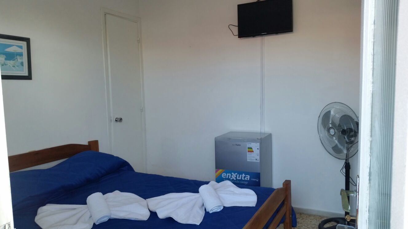 A room with a bed, a TV mounted on the wall, a heater, and a fan.