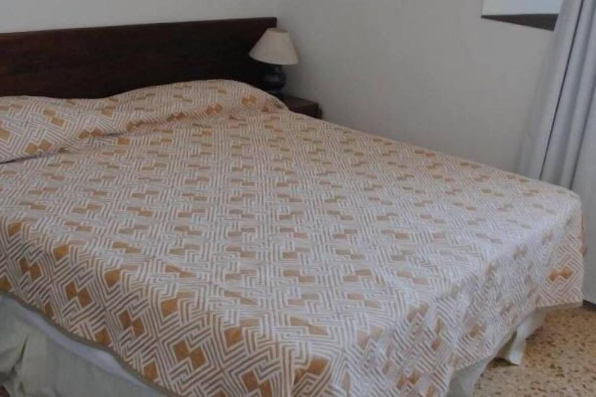 Ein Bett mit gemustertem Überwurf, einem Holzkopfteil und einem Nachttisch mit Lampe.