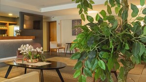A modern living room with a sofa, coffee table, and a potted plant. - Hotel Querência (Gramado)