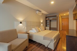 A modern hotel room with a bed, a sofa, a wardrobe, and an air conditioning unit. - Hotel Querência (Gramado)