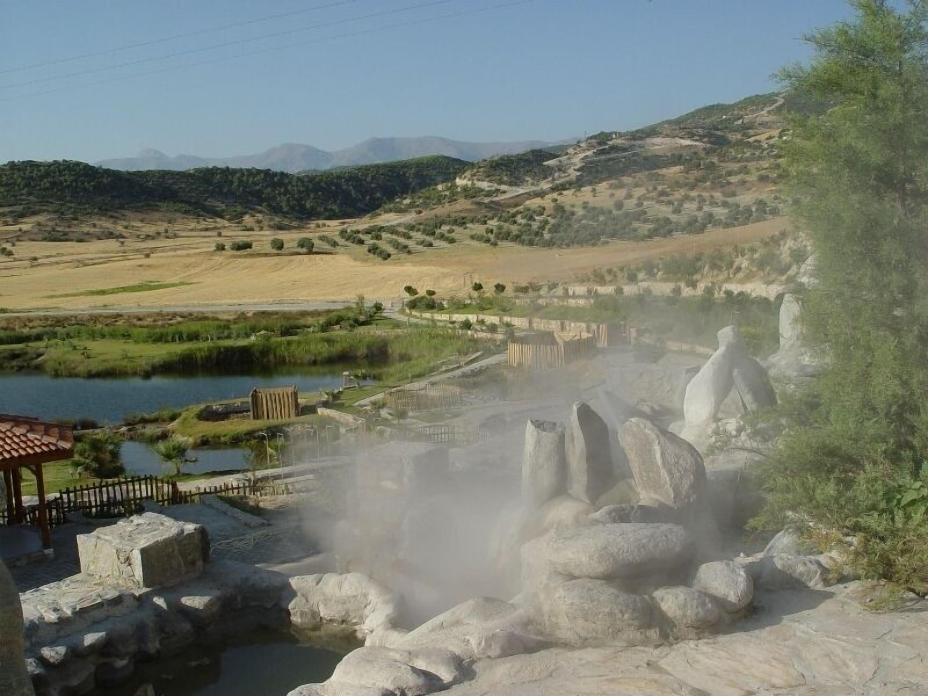 A geothermal area with steam vents, a small pond, and a wooden fence.