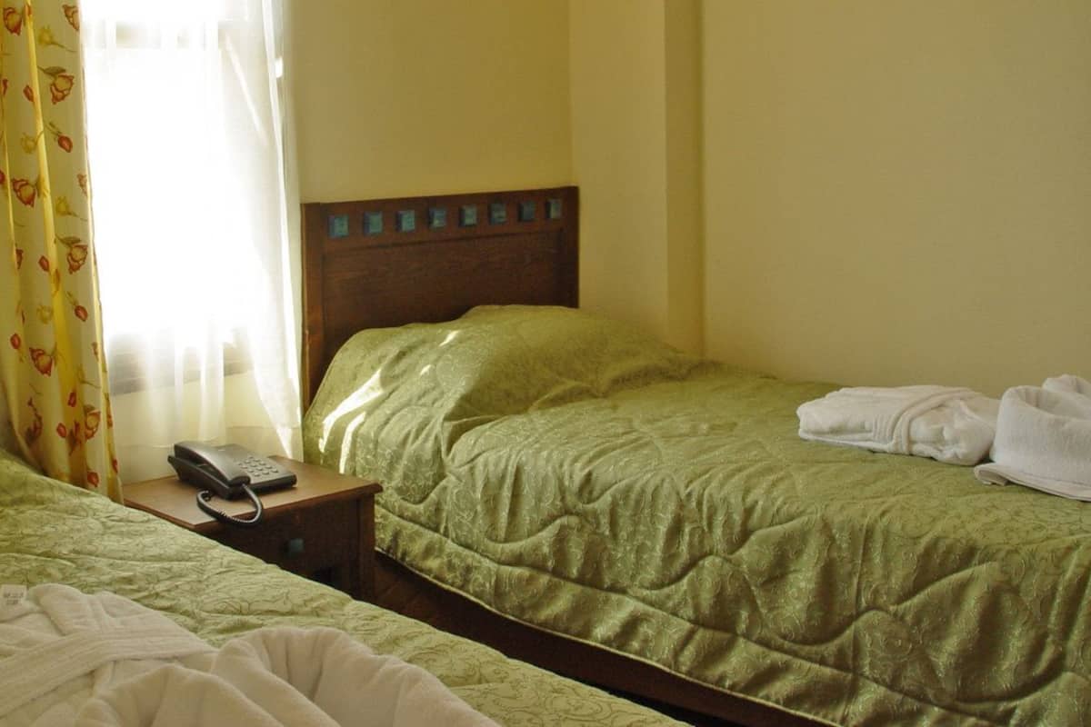 Een hotelkamer met twee enkele bedden, een nachtkastje met telefoon en een raam met gordijnen.