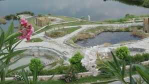 Uma área ajardinada com vários lagos e caminhos para passear, rodeada por vegetação e estruturas de pedra.