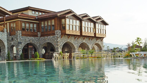 Um hotel com fachada de pedra, várias varandas e área de piscina com espreguiçadeiras.