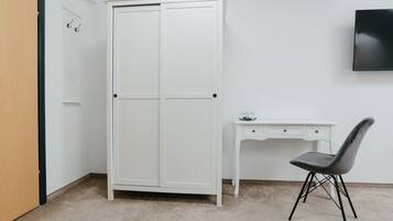 A room with a white wardrobe, a desk with a chair, and a wall-mounted TV.