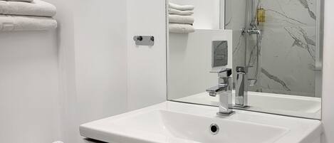 A modern bathroom with a white sink, a mirror, a shower, and neatly folded towels on a rack.