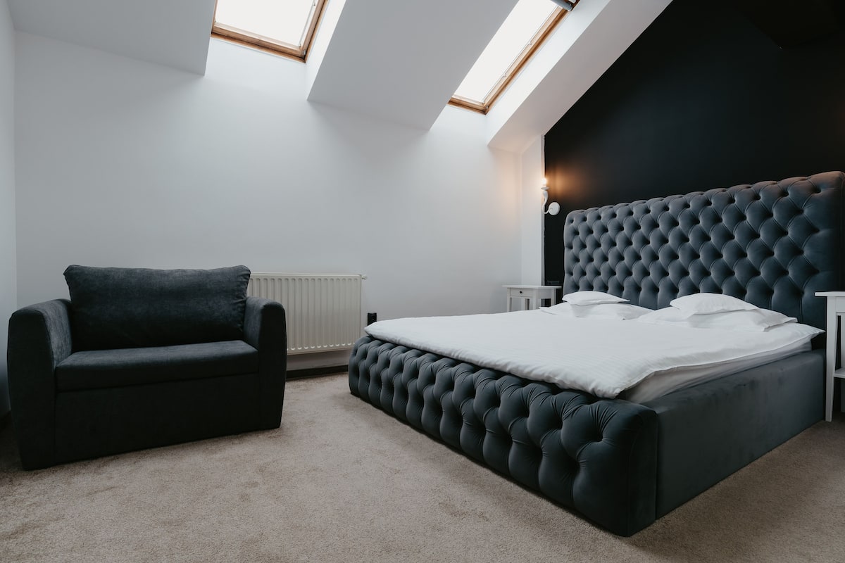 A modern bedroom with a tufted headboard bed, a dark sofa, and skylights.