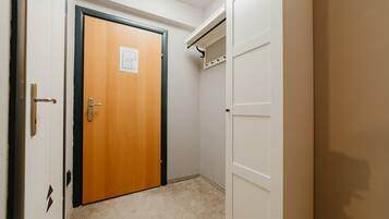 A hallway with a wooden door, a white closet with a hanging rod, and a carpeted floor.