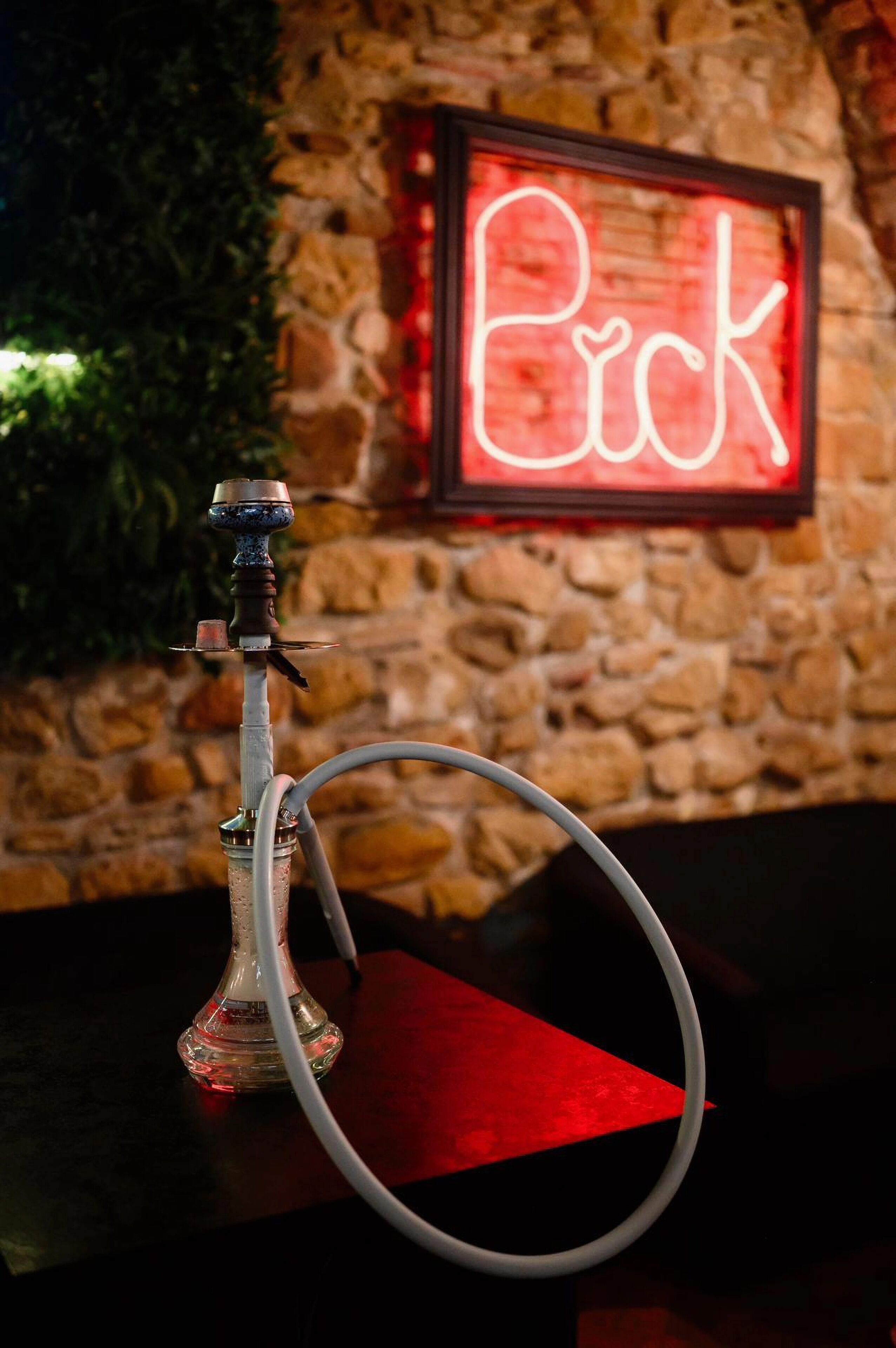 A hookah with a red neon sign in the background.