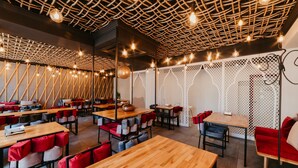 A modern restaurant with wooden tables and red cushioned chairs, a woven ceiling design, and string lights. - Fullton Central Inn (Cluj-Napoca)