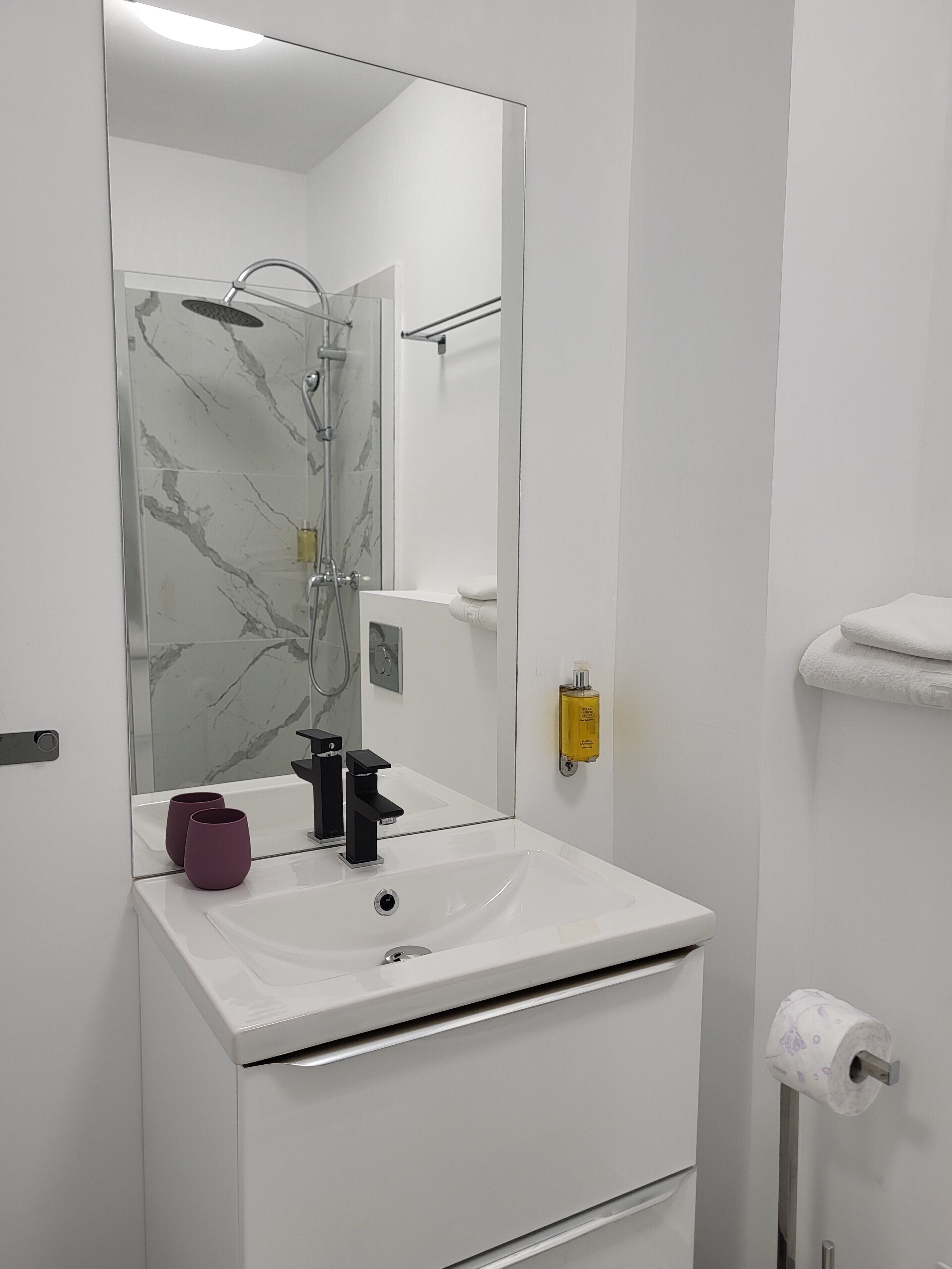 A bathroom with a white sink, a mirror, a shower, and a towel rack.