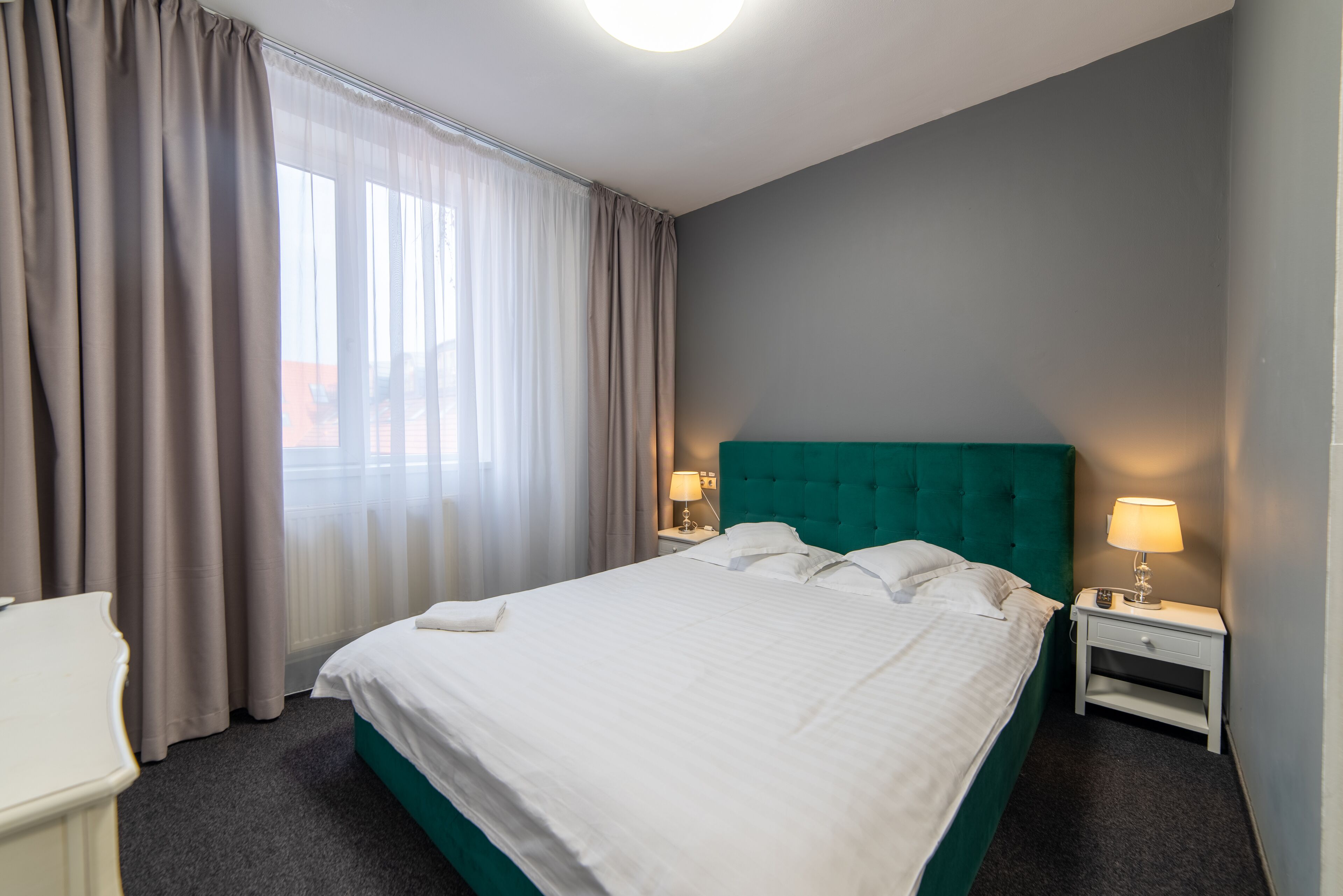 Una habitación de hotel con una cama grande, dos mesitas de noche con lámparas, un escritorio y una ventana con cortinas.